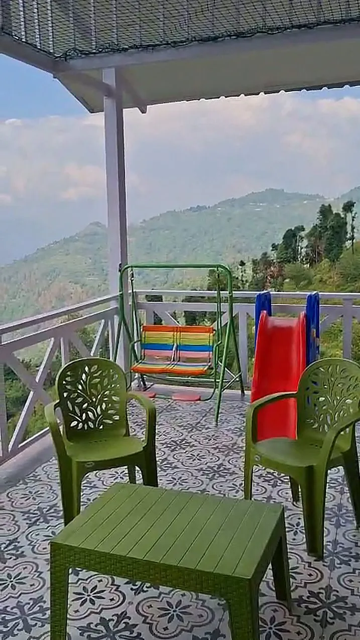 A tiled deck with chairs, a swing and a slide facing the hills